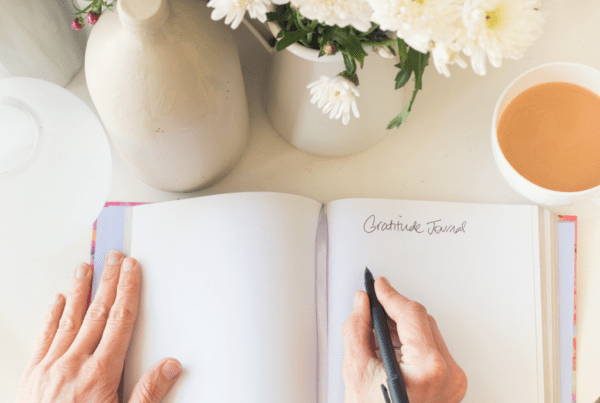 Hands pen writing in gratitude journal with coffee and flowers