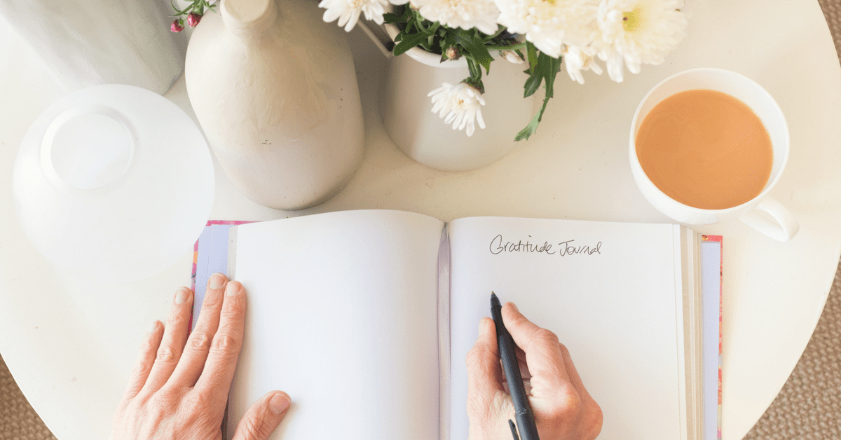 Hands pen writing in gratitude journal with coffee and flowers